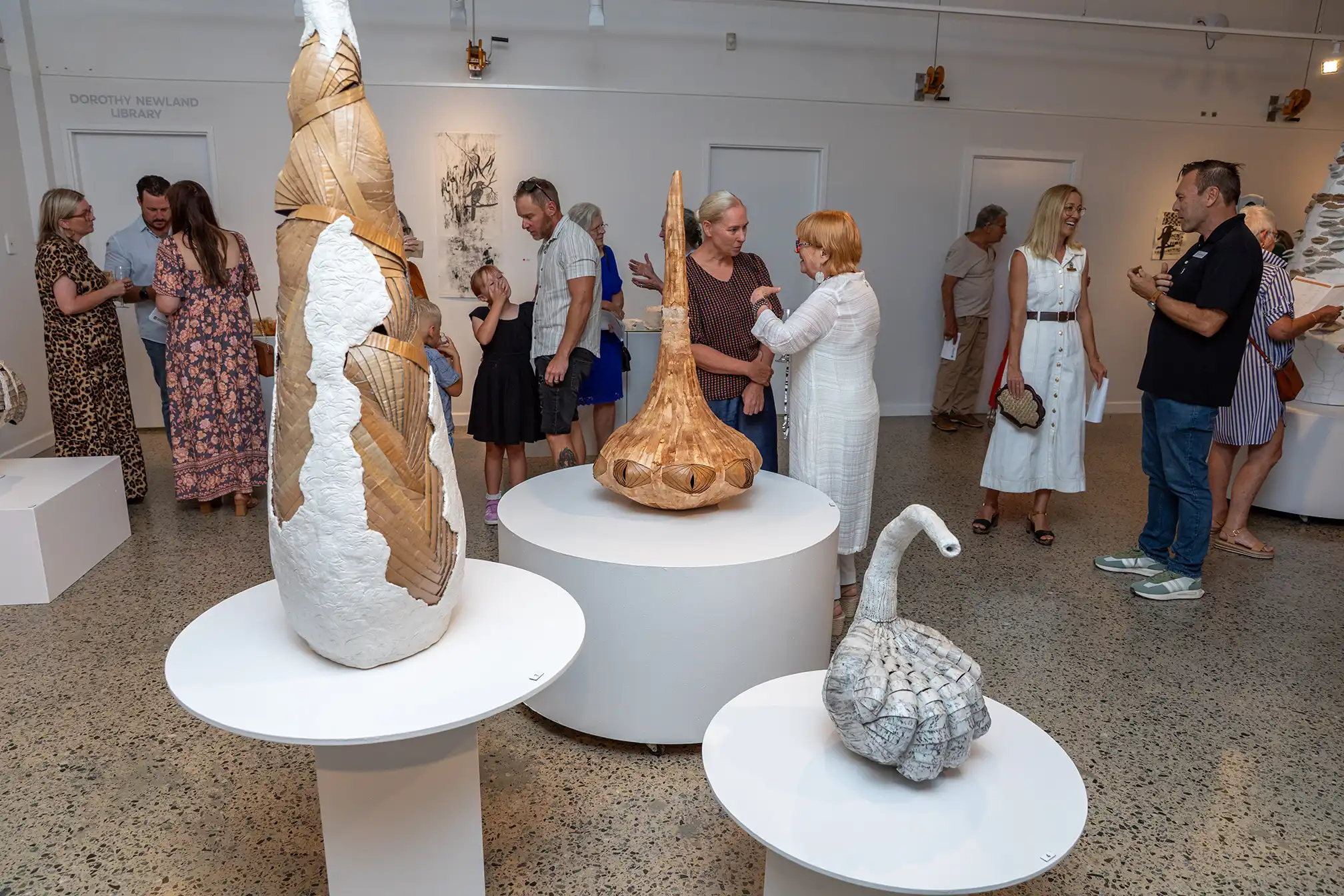 Art gallery exhibition with ceramic sculptures displayed on plinths and visitors viewing the artworks.